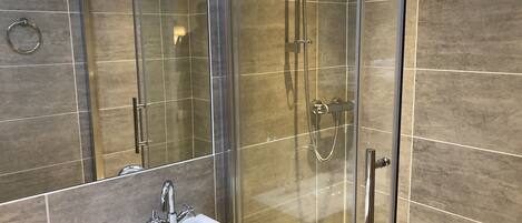 Un baño moderno con ducha envuelta en vidrio, un lavamanos con espejo y paredes de azulejos.