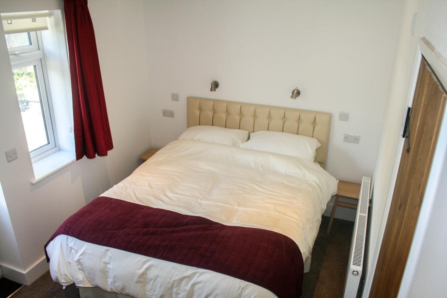 Un letto singolo con una testiera beige, biancheria da letto bianca e una tenda rossa.