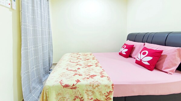 A bed with a floral bedspread and two red pillows with white designs, a grey headboard, and a light-colored wall.