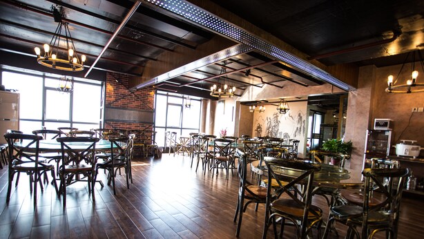 Un restaurante espacioso con techos altos, paredes de ladrillo visto y diversas opciones de asientos, incluyendo mesas y sillas.