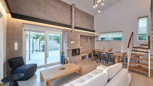 A modern living room with a fireplace, a sofa, a dining area, and a staircase. - Suitable For Families With Children, Groups Of Friends, Professionals, Friends (Rethimno)