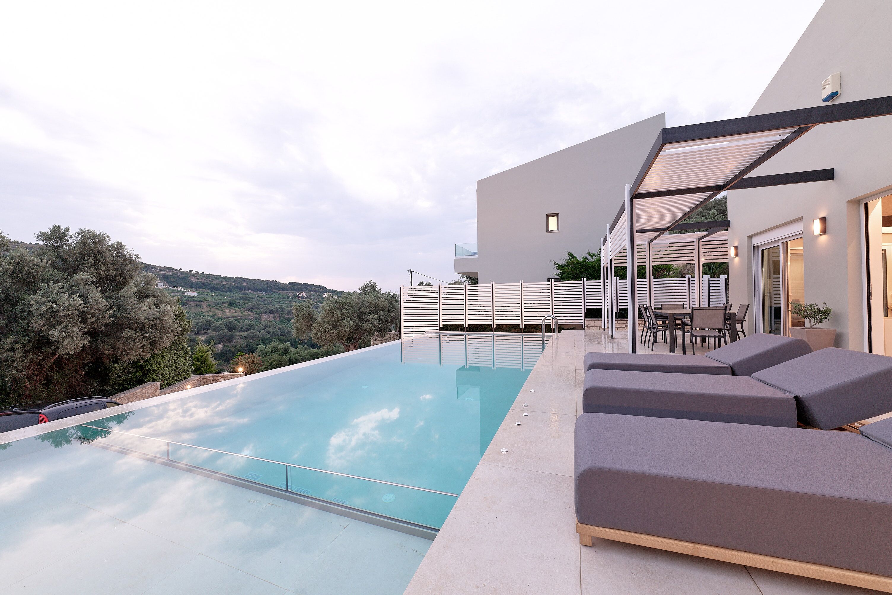 Un espace piscine extérieur moderne offrant une vue dégagée sur le paysage environnant, un coin salon avec des coussins et un espace repas aménagé.