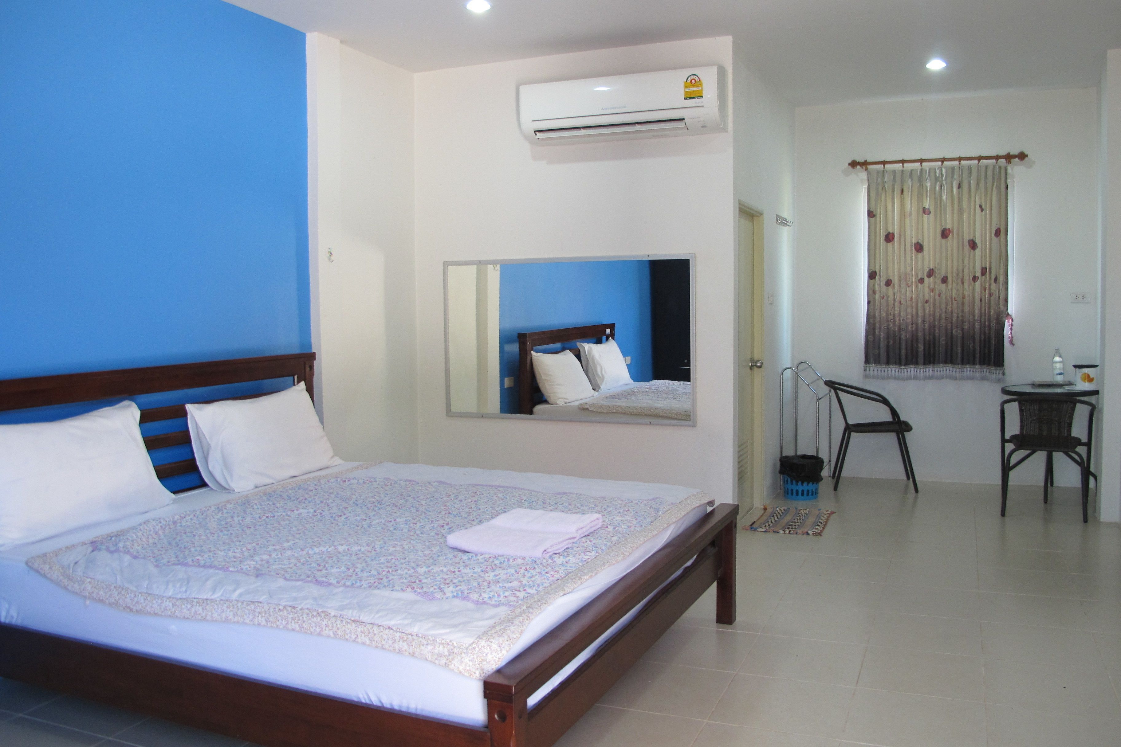 A bedroom with a bed, a mirror, an air conditioner, a chair, and a small table.