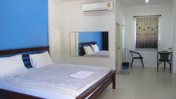 A bedroom with a bed, a mirror, an air conditioner, a chair, and a small table.