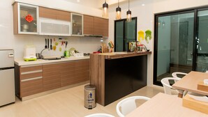 A modern kitchen with wooden cabinets, a built-in microwave, and a dining area with a wooden table and chairs. - Fat Snail BnB (Tainan)