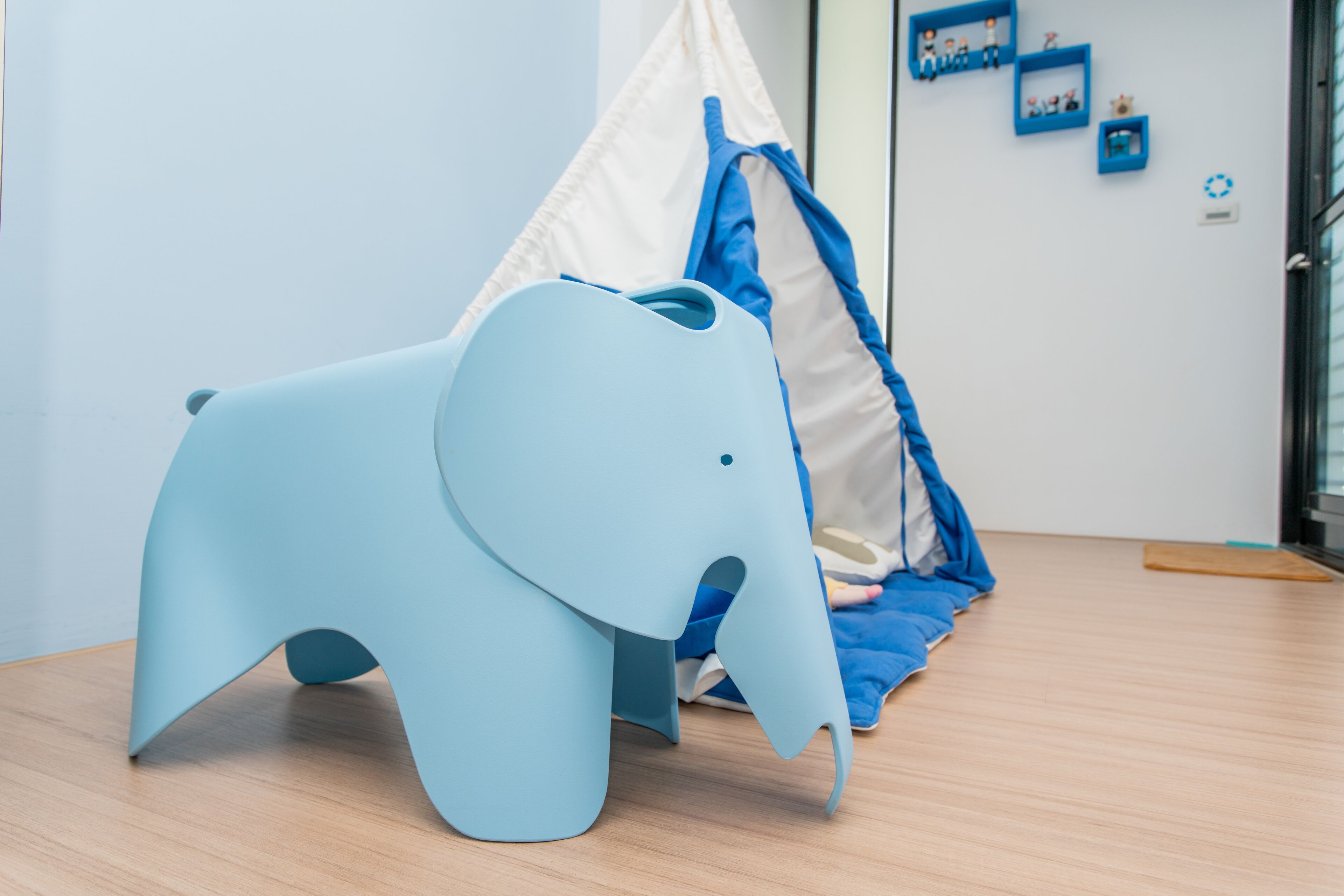 Una habitación con una silla en forma de elefante azul, una estructura tipo tienda blanca y suelo de madera.