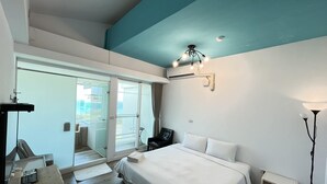 A hotel room with a bed, a desk, a chair, a lamp, and a view through a glass door. - Cest la vie B&B (Hengchun)
