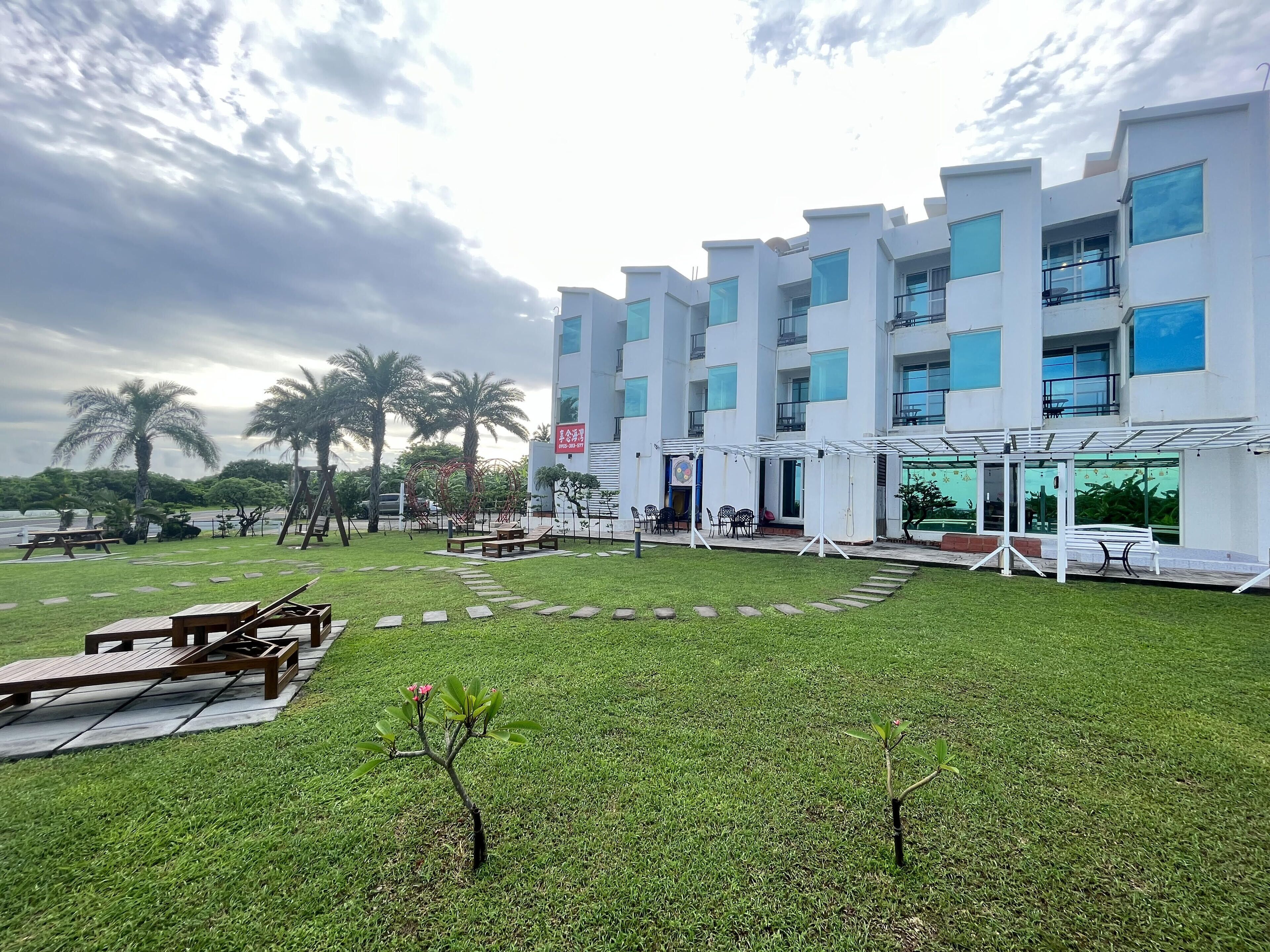 Un hotel moderno con un patio que cuenta con asientos al aire libre, palmeras y un cielo despejado.