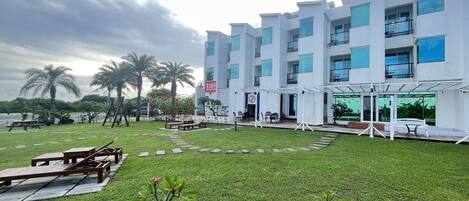 Un hotel moderno con un patio que cuenta con asientos al aire libre, palmeras y un cielo despejado.