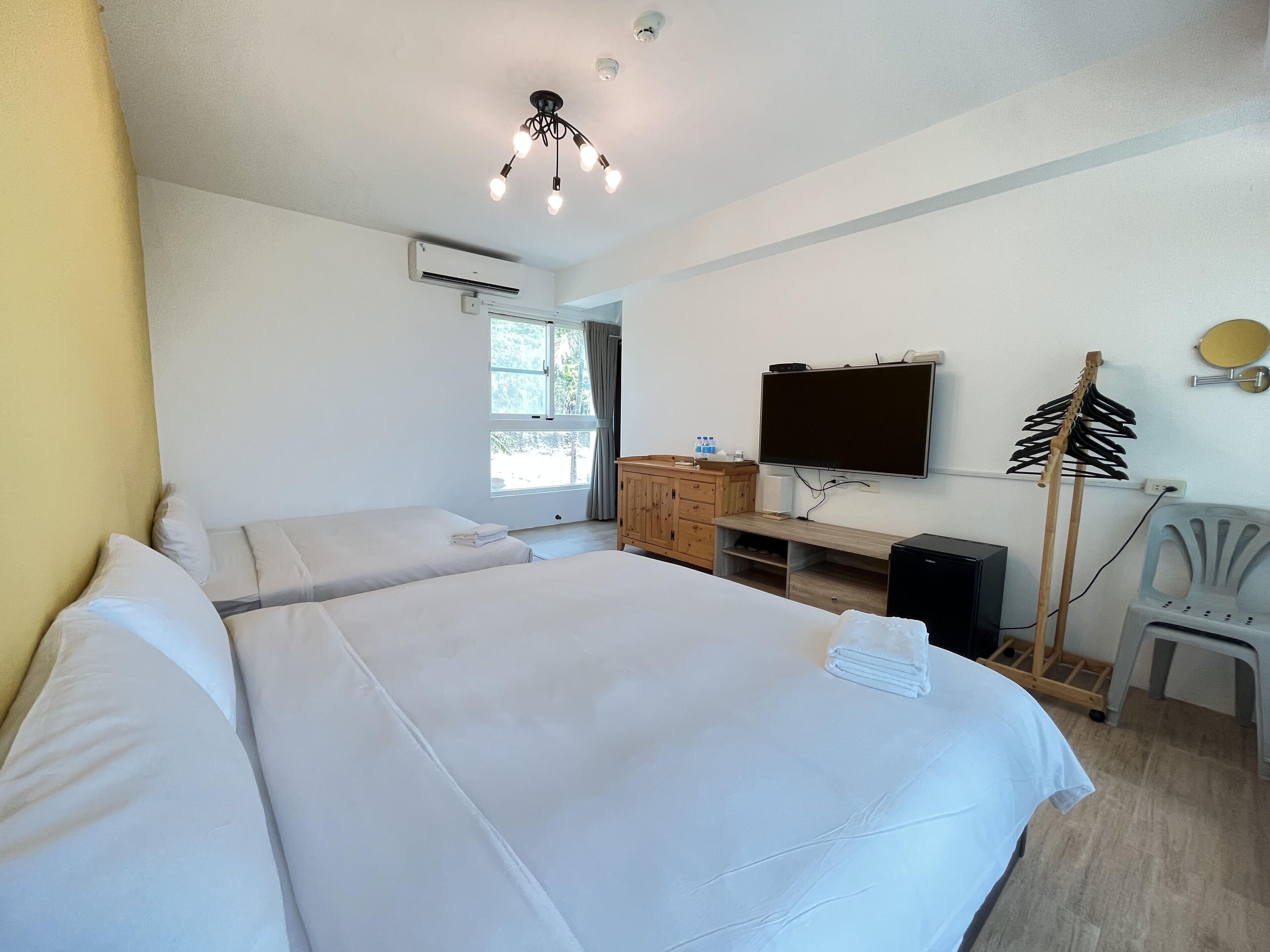 A hotel room with two beds, a TV, a wooden cabinet, and a desk.