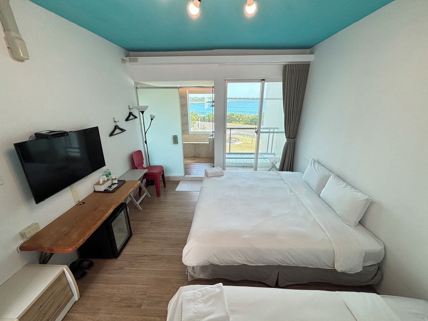 A hotel room with a bed, a TV, a desk, and a view of the sea.