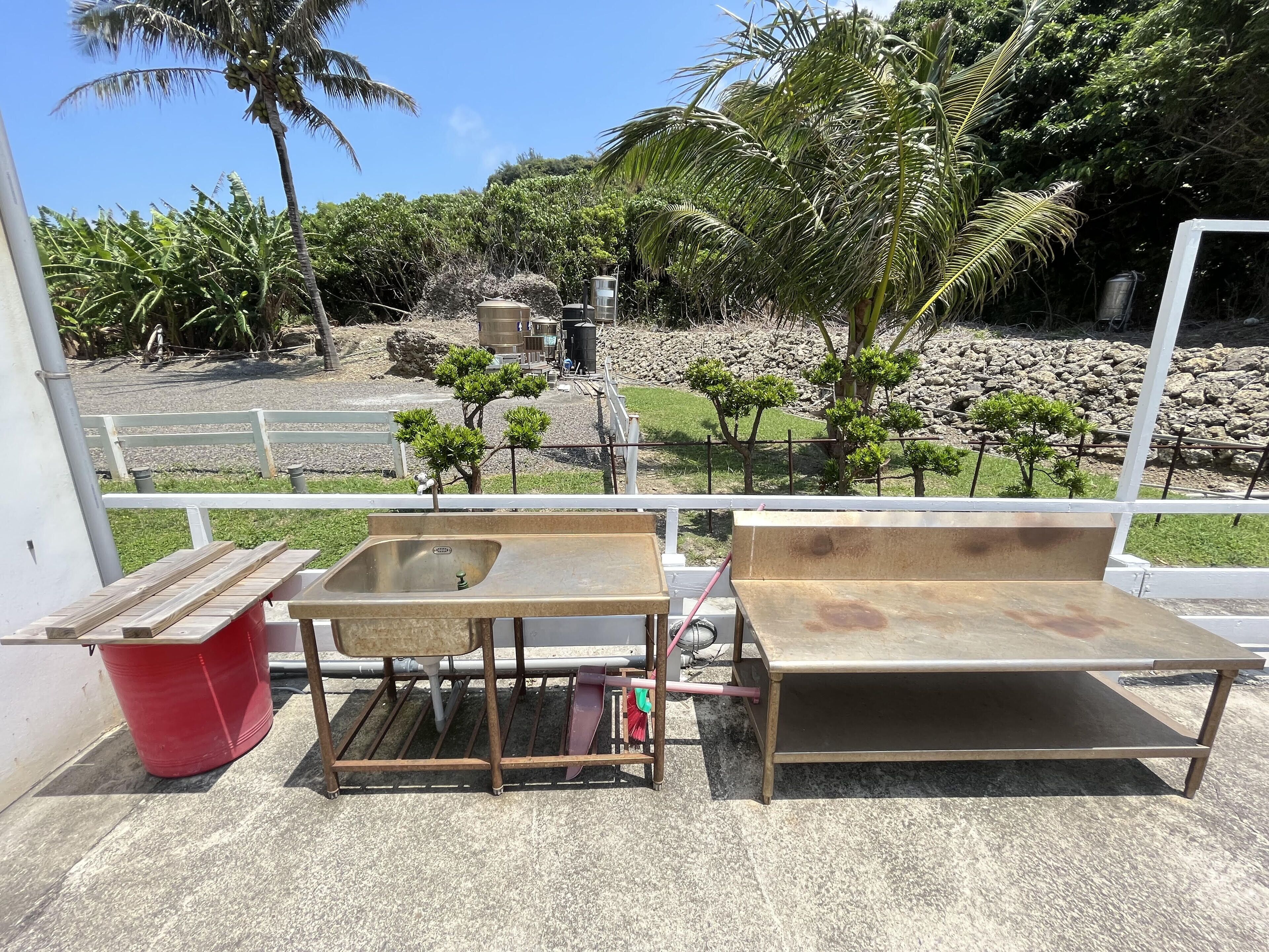 A balcony with a metal sink, a red trash bin, and a wooden bench.