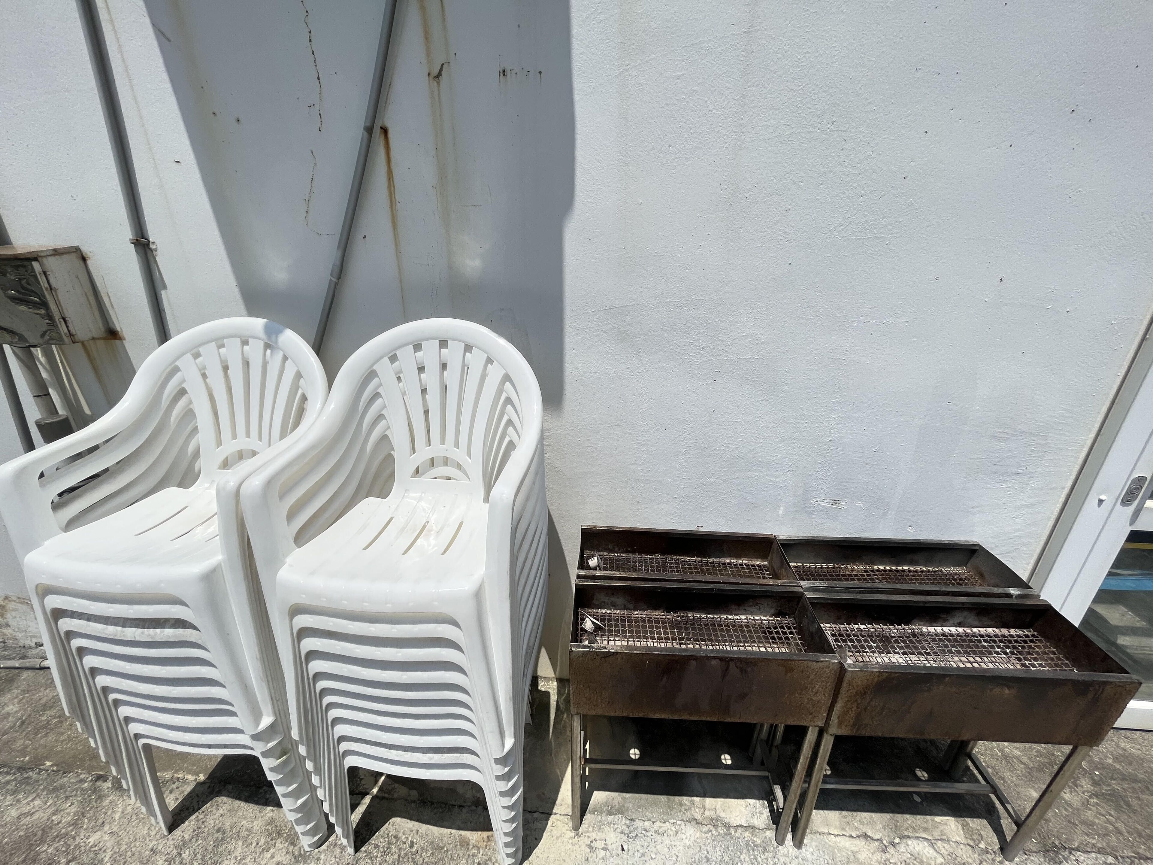 Een stapel witte plastic stoelen en een metalen barbecue.