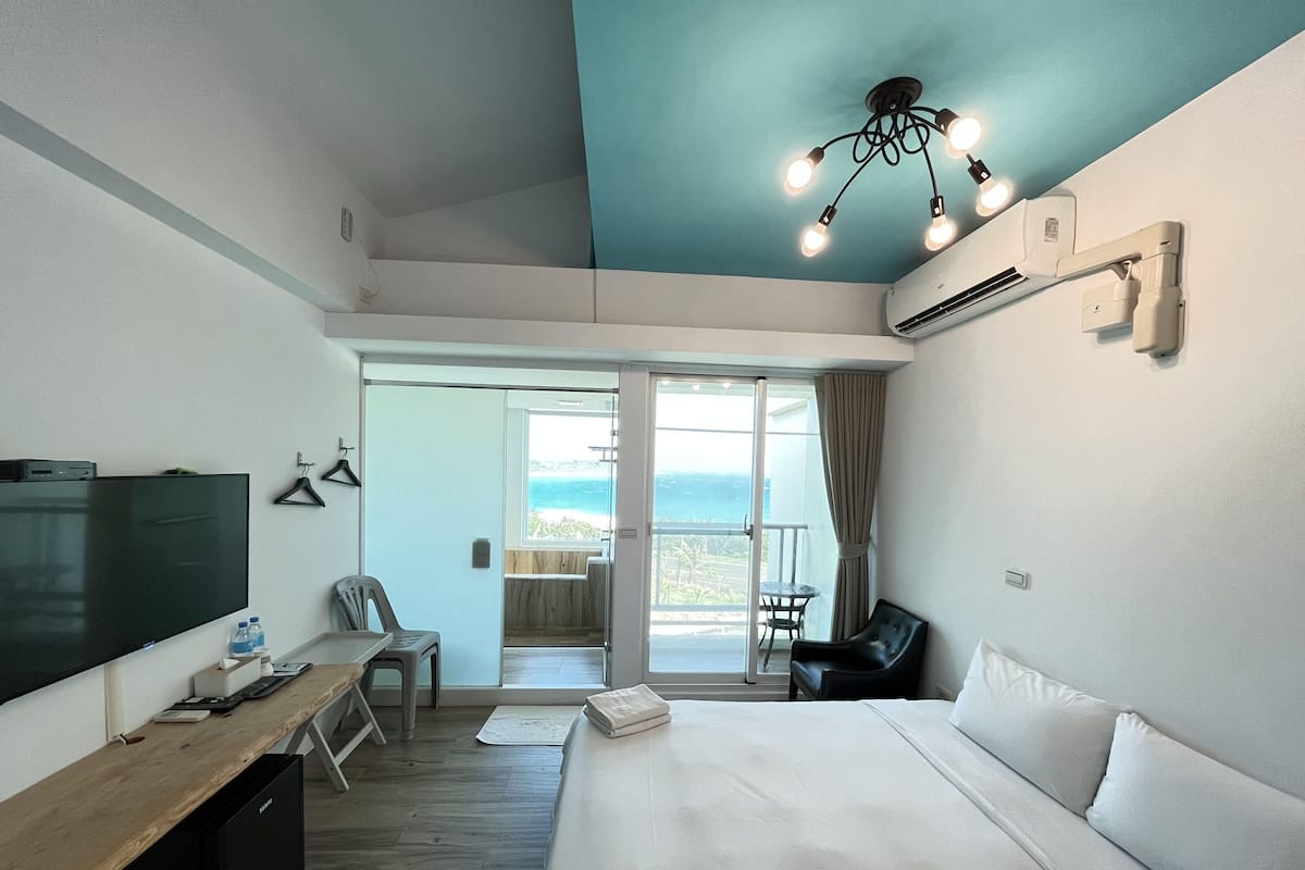 A hotel room with a bed, a desk, a TV, a chair, and a balcony with a view.
