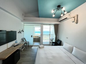 A hotel room with a bed, a desk, a TV, a chair, and a balcony with a view. - Cest la vie B&B (Hengchun)