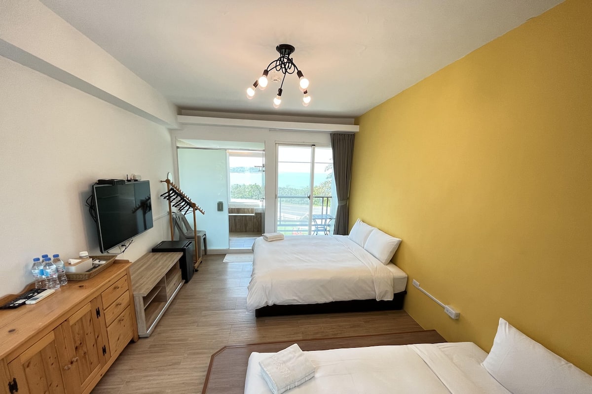 A hotel room with two beds, a TV, a wooden dresser, and a balcony with a view.