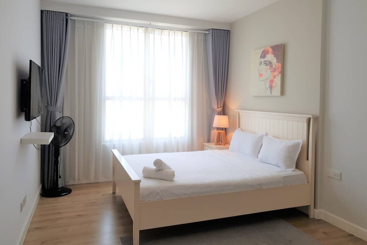 Quarto bem arrumado com uma cama, uma televisão na parede, um ventilador e um abajur.