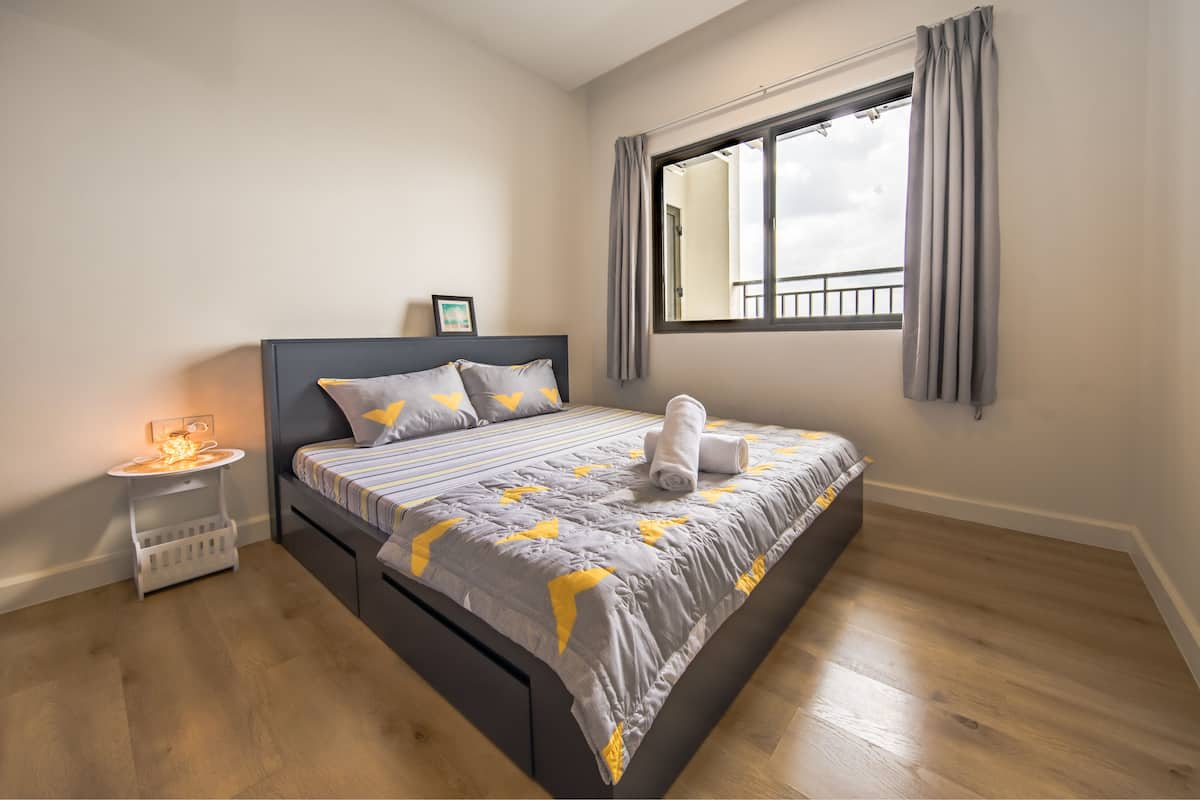 Quarto com cama, mesa de cabeceira e janela com cortinas.