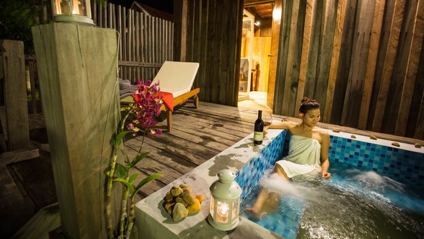 A wooden deck with a hot tub, a lounge chair, and a table with rocks and a bottle of wine. - Kampot River Residence (Kampot)