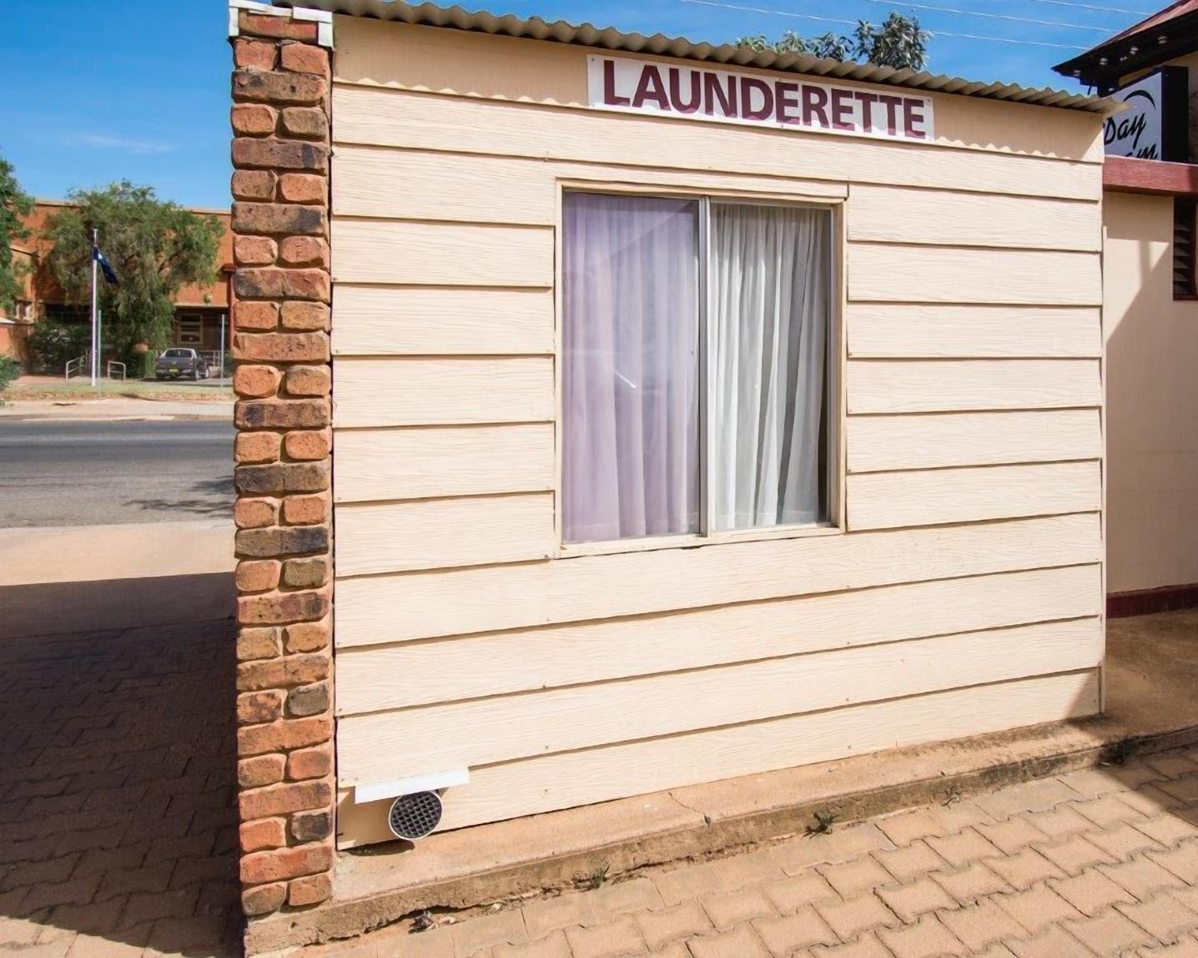 A laundrette with a brick exterior, a window with curtains, and a sign above the window.