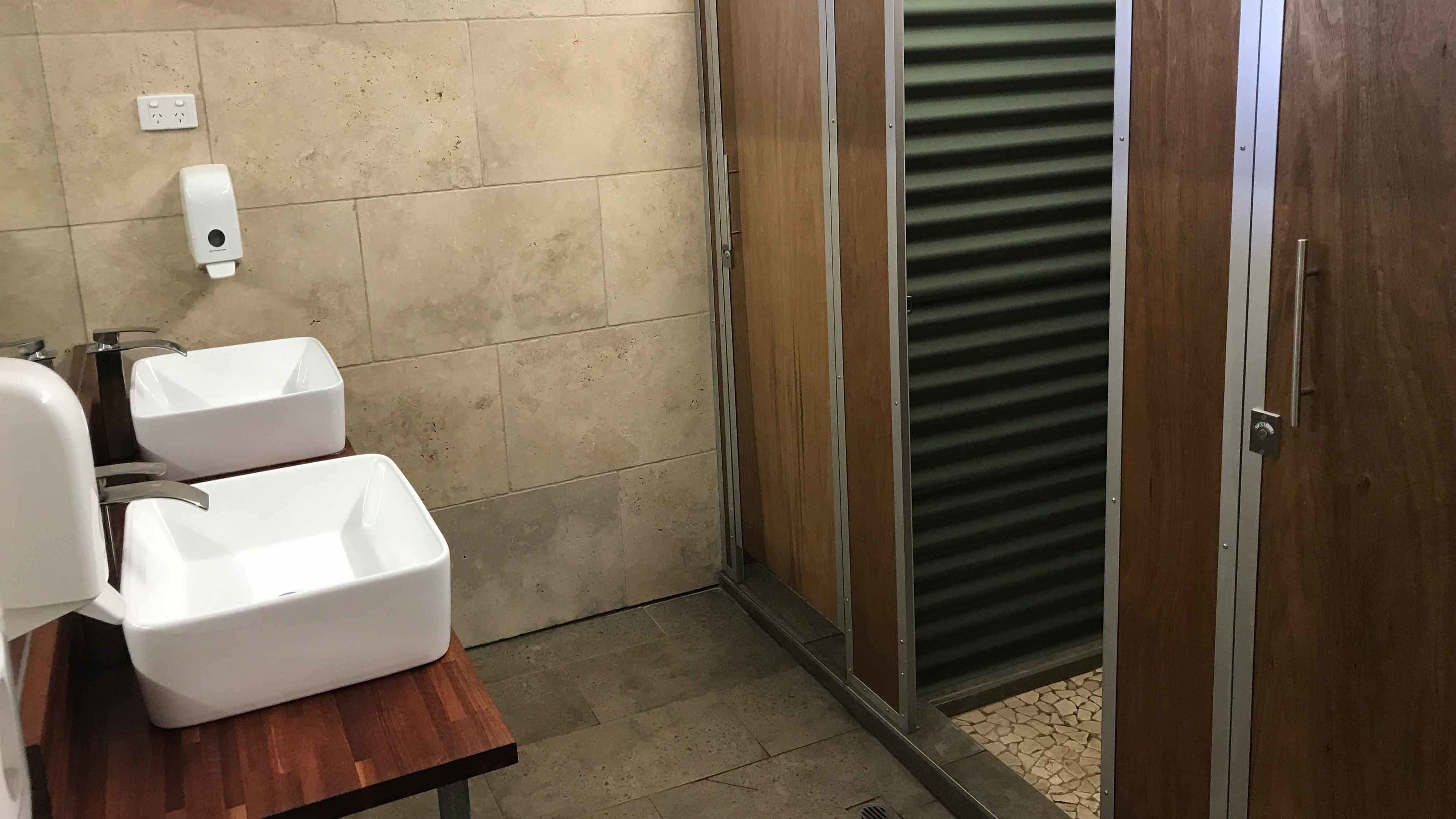 Ein Badezimmer mit zwei Waschbecken, einer Seifenspender und einer hölzernen Sitzbank.