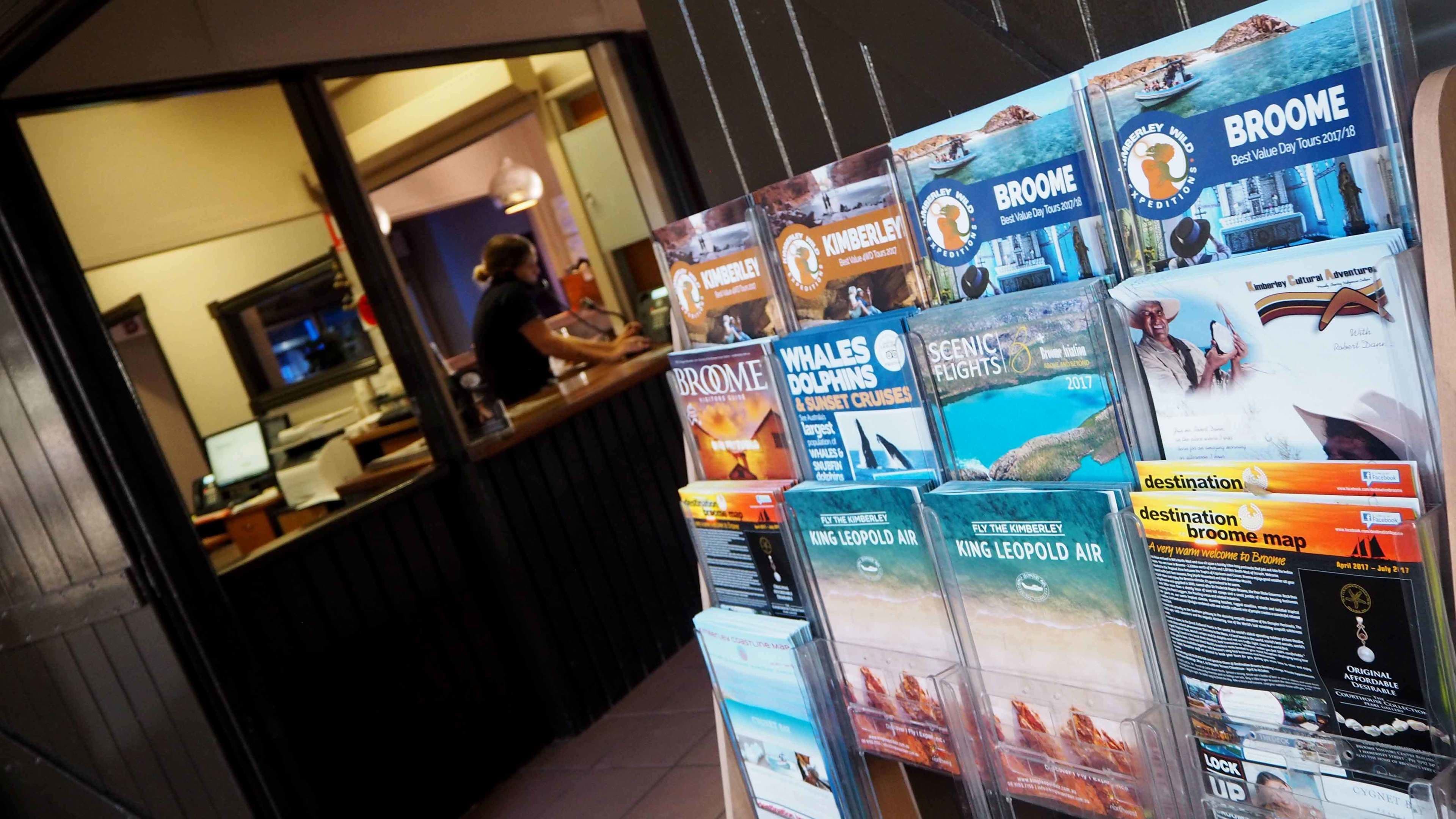 Une agence de voyages présente des brochures sur les circuits touristiques de Broome et de Kimberley, notamment des destinations où l’on peut observer des baleines, des dauphins et profiter de vols panoramiques.