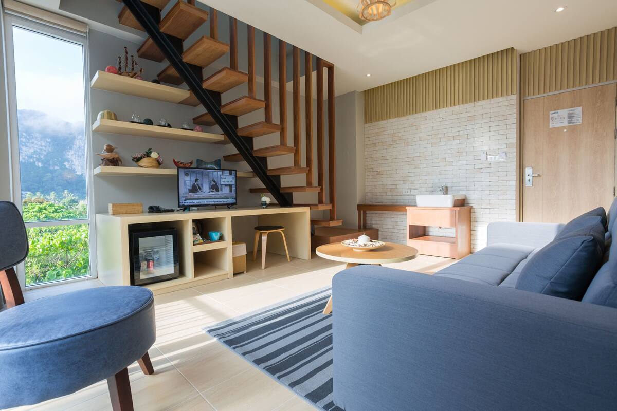 Una sala de estar moderna con una escalera, un televisor y vistas al verdor.