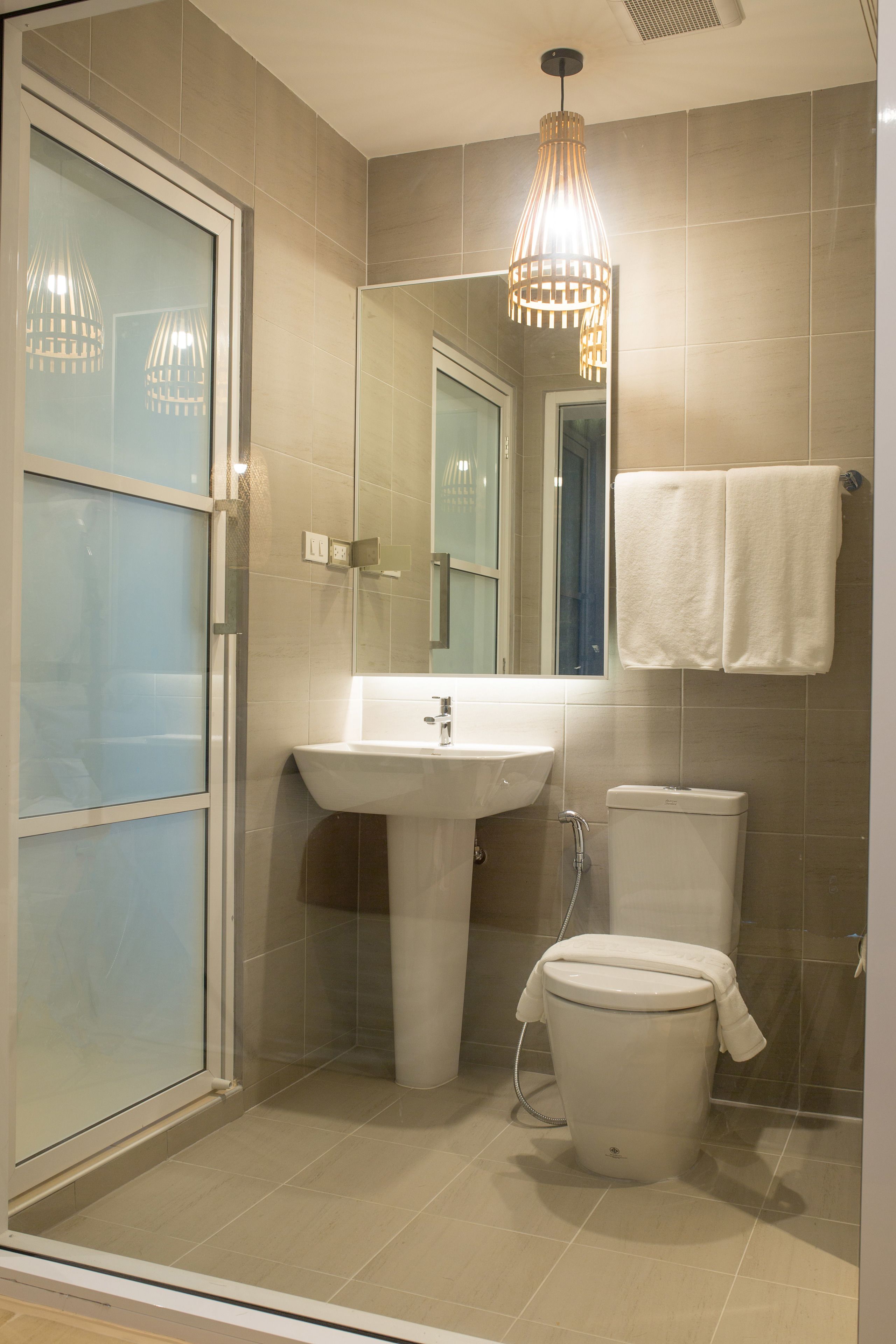 Un baño moderno con cabina de ducha de vidrio, lavamanos pedestal, inodoro y lámpara colgante.