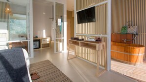A modern hotel room with a large bed, a TV, a wooden vanity, and a bathtub.