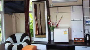 A room with a bed, a desk with a refrigerator, a TV mounted on the wall, and a window with curtains.