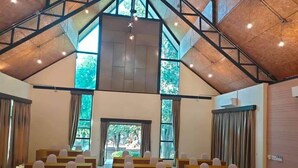 A conference room with rows of desks and chairs, large windows, and a high ceiling with exposed beams.