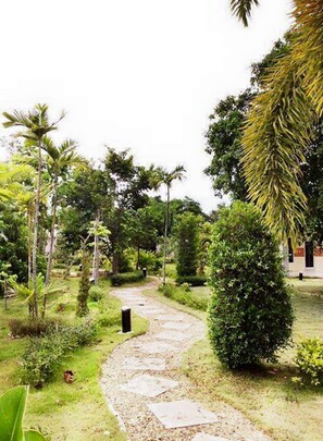 A stone pathway winding through a lush garden with various trees and shrubs. - Nan at Pua (Pua)