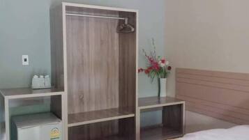 A hotel room with a bed, a wardrobe, a small fridge, a bedside table, and a potted plant.