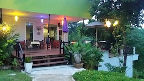 An outdoor patio area with a covered seating area, potted plants, and a pathway leading to the entrance.