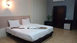A neatly made bed with a white comforter and pillows, a bedside table with a lamp, and a wall-mounted air conditioner.