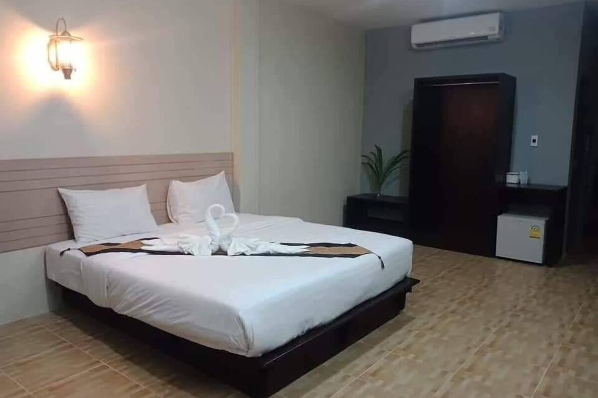 Una cama bien hecha con edredón blanco y almohadas, una mesita de noche con lámpara y un aire acondicionado de pared.