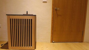 A wooden speaker unit with a vertical grille design, positioned on a wooden floor next to a wooden door. - Stay Resort (Fenglin)