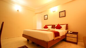 A neatly made bed with red pillows, a bedside table with a phone, and a small rug on the floor. - Citadel by New Crescent (Bengaluru)