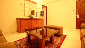 A living room with a glass-top coffee table, a sofa, a patterned rug, a wooden cabinet, and a mirror on the wall. - Citadel by New Crescent (Bengaluru)