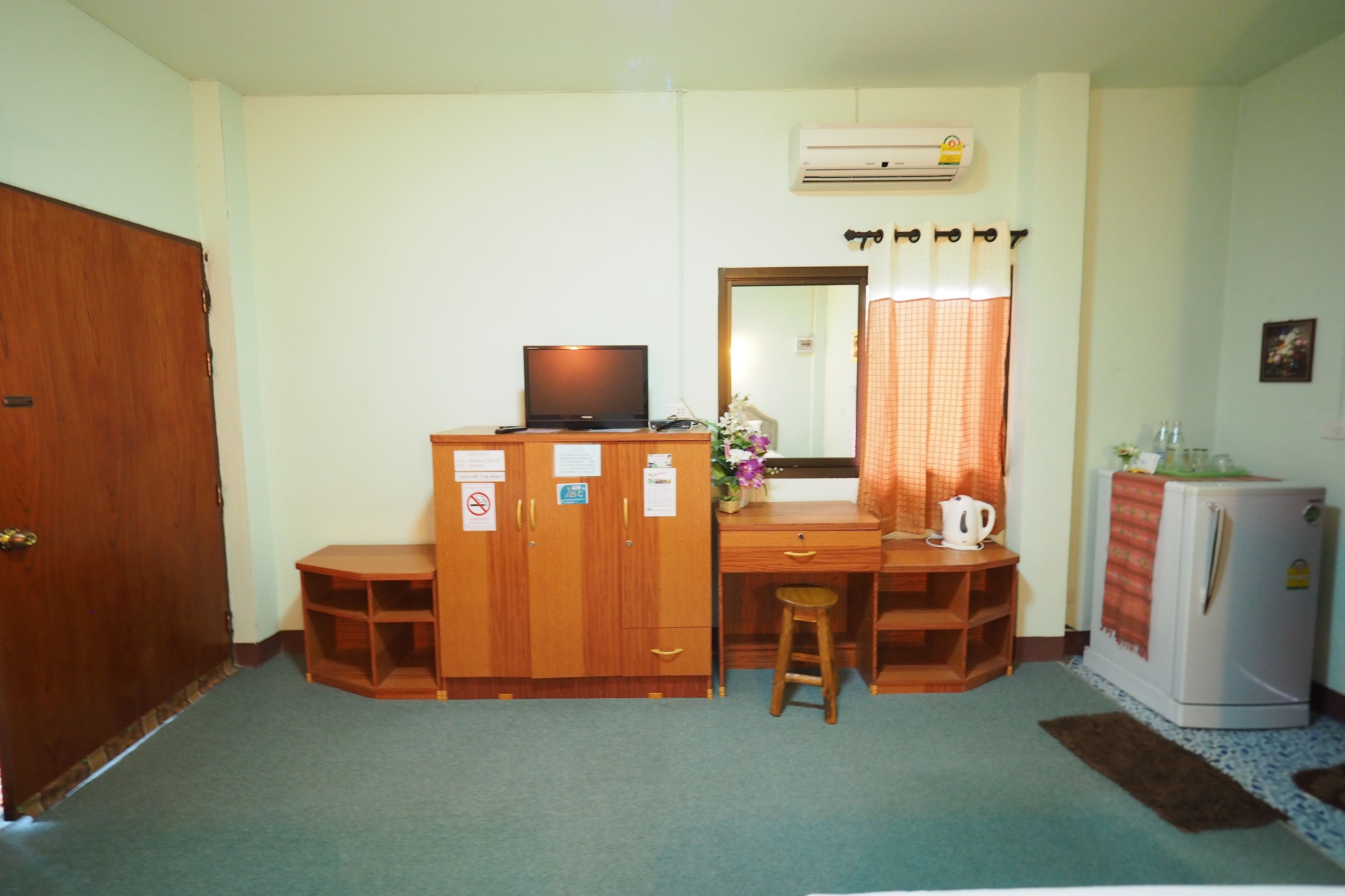 A small room with a wooden desk, a television, a refrigerator, and a mirror.