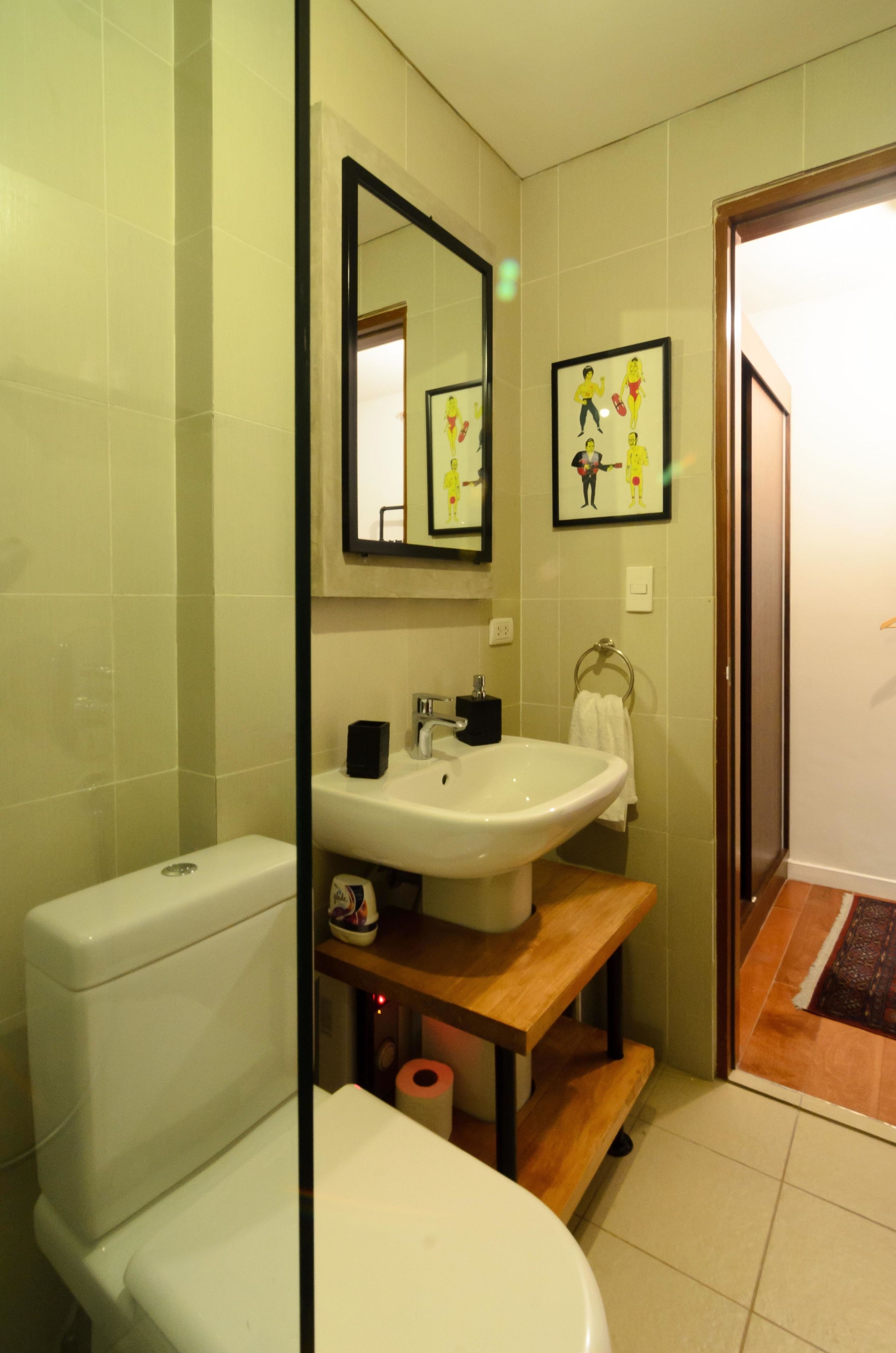 Un baño con inodoro, lavamanos y espejo. Hay un perchero para toallas y un dispensador de papel higiénico.