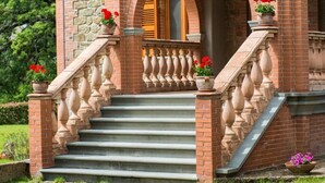 A two-story building with a stone facade, a balcony with balustrades, and a staircase leading to the entrance. - San Bartolomeo LT (Passignano sul Trasimeno)