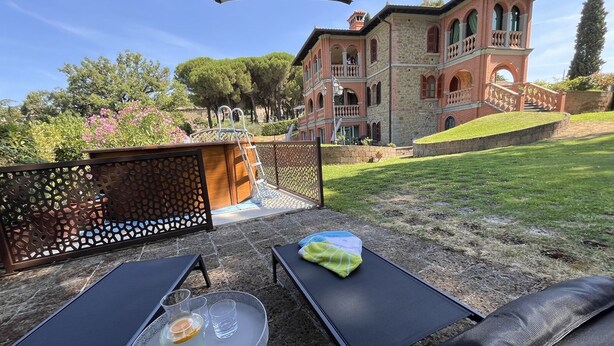 A patio with two lounge chairs, a small table with a pitcher and glasses, and a decorative fence. - San Bartolomeo LT (Passignano sul Trasimeno)