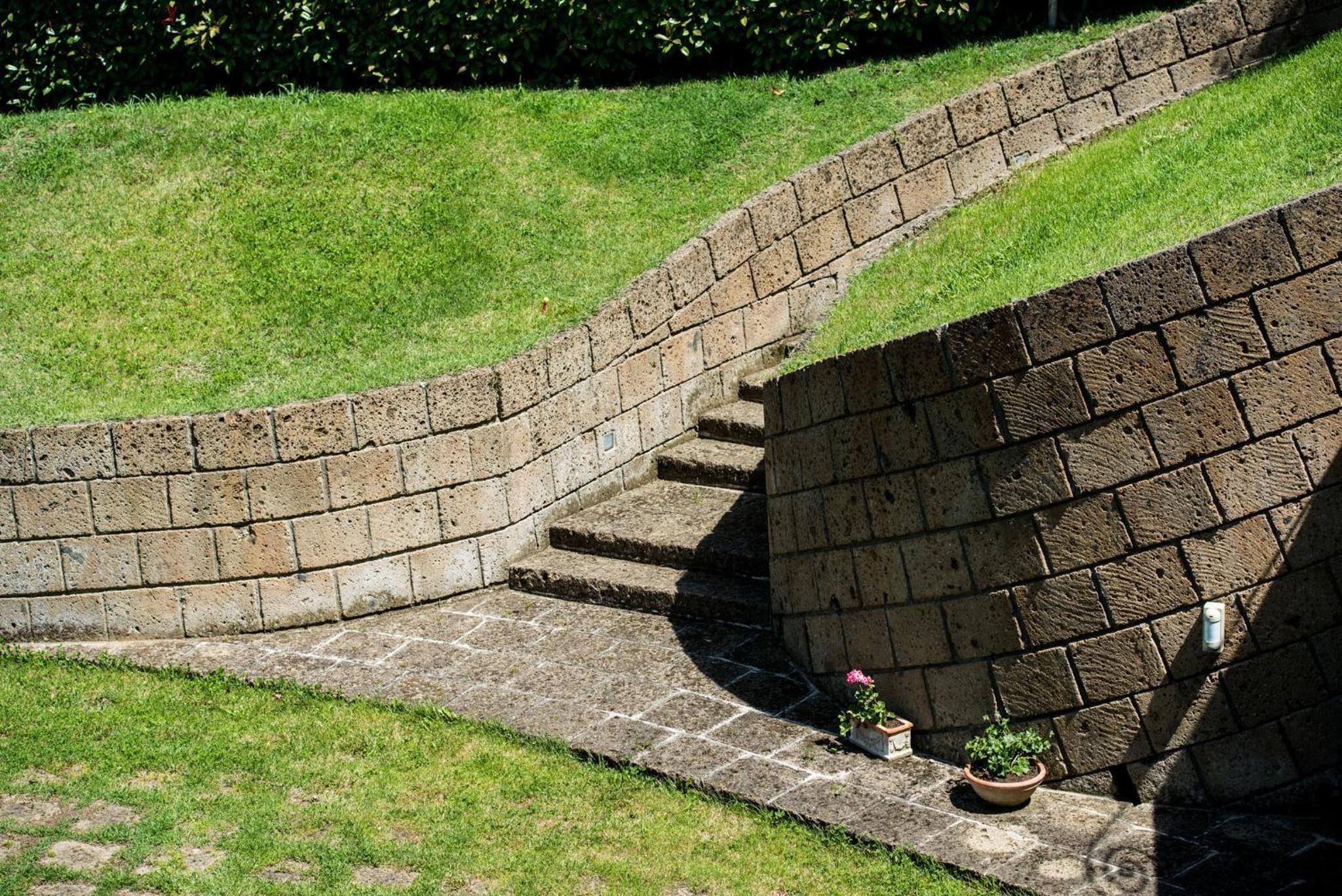 Eine Steintreppe führt zu einer Backsteinmauer, am Fuß befindet sich ein kleiner Blumentopf.