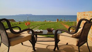 Un patio con mobiliario de mimbre y una mesa de vidrio, con vistas a una zona verde y al mar.