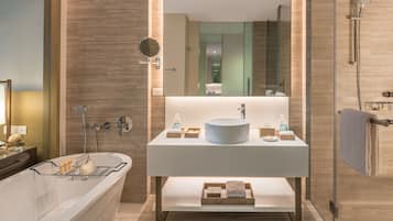 A modern bathroom with a freestanding bathtub, a large mirror, and a vanity with a round sink and wooden storage.