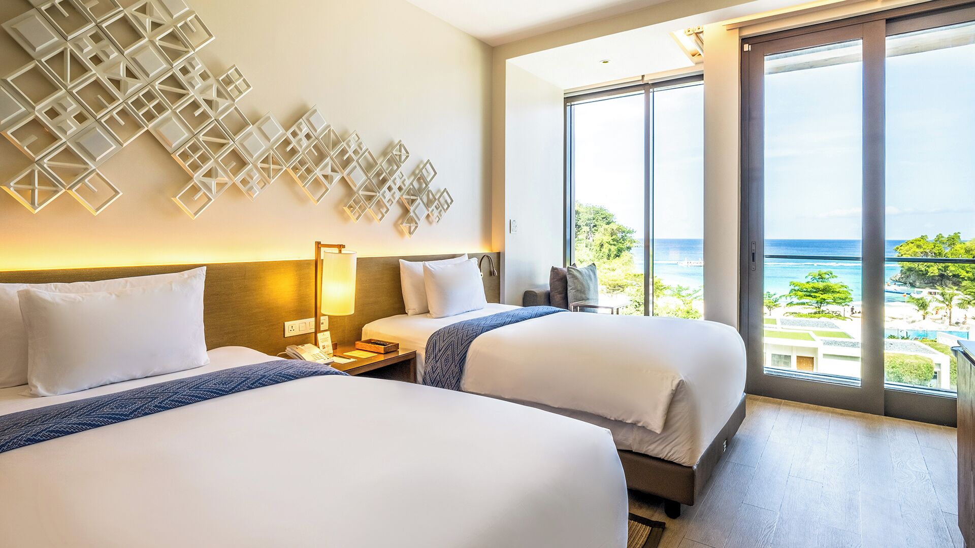 A hotel room with two beds, a large window with a view of the ocean, and a decorative wall panel.