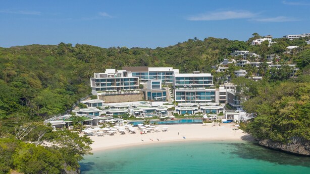 Un resort con varias construcciones, una playa y aguas turquesas cristalinas.