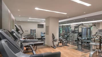 Une salle de sport moderne équipée de divers appareils d’exercice, notamment des tapis de course et des appareils de musculation, ainsi qu’un grand mur entièrement recouvert de miroirs.