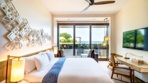 Habitación de hotel con una cama grande, un escritorio, un televisor y un balcón con vista al océano.